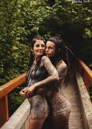 Сильно татуированные лесбиянки обнимают друг друга, будучи полностью обнаженными на мосту
